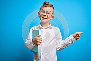 Young little caucasian student kid wearing smart glasses and holding a book from school very happy pointing with hand and finger