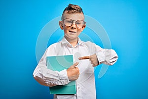 Young little caucasian student kid wearing smart glasses and holding a book from school very happy pointing with hand and finger