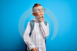 Young little caucasian student kid wearing smart glasses and school bag over blue background with hand on chin thinking about