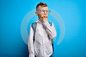Young little caucasian student kid wearing smart glasses and school bag over blue background looking stressed and nervous with