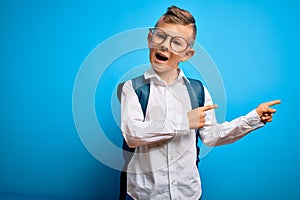 Young little caucasian student kid wearing smart glasses and school bag over blue background smiling and looking at the camera