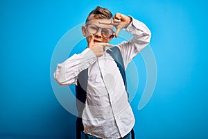 Young little caucasian student kid wearing smart glasses and school bag over blue background smiling making frame with hands and