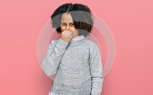 Young little girl with afro hair wearing casual clothes smelling something stinky and disgusting, intolerable smell, holding