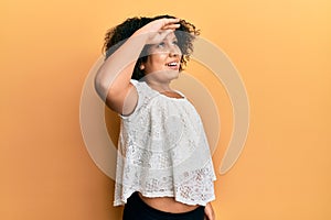 Young little girl with afro hair wearing casual clothes very happy and smiling looking far away with hand over head