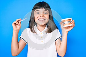 Young little girl with bang holding invisible aligner orthodontic and braces smiling with a happy and cool smile on face photo