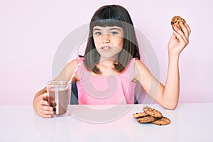 Young little girl with bang sitting on the table having breakfast clueless and confused expression