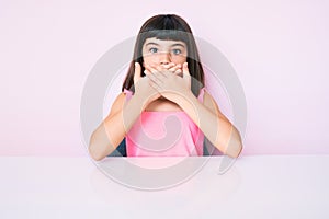 Young little girl with bang wearing casual clothes sitting on the table shocked covering mouth with hands for mistake