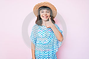 Young little girl with bang wearing summer dress and hat smiling happy and positive, thumb up doing excellent and approval sign