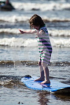 Young little girl on beach taking surfing lessons