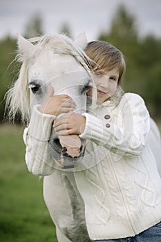 Young little girl embraces a white horse over the head. Lifestyle portrait