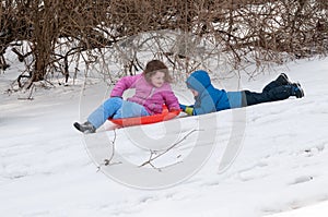 Young little girl enjoying sledding outside on a snow day while her brother holds onto the back dragging along after her