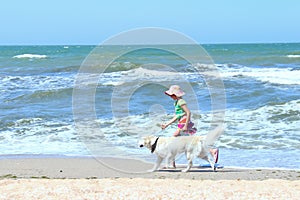 Young Little Girl And Golden Retriever Dog Running On The Beach. Dog And Owner Outdoors.