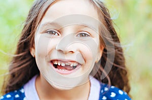 Young little girl with long hair without front tooth smiles, natural light