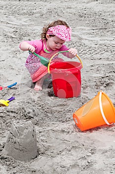 Young little girl playing with the sand and building sandcastle at the beach near the sea.