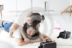 Young little girl sitting on her mother`s back and playing with each other in living room