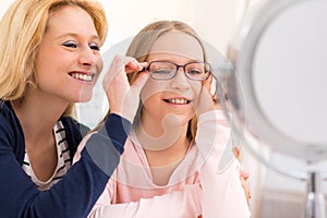 Young little girl trying glasses at the optician w her mother