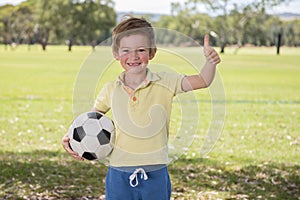 Young little kid 7 or 8 years old enjoying happy playing football soccer at grass city park field posing smiling proud standing ho