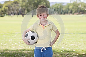 Young little kid 7 or 8 years old enjoying happy playing football soccer at grass city park field posing smiling proud standing ho