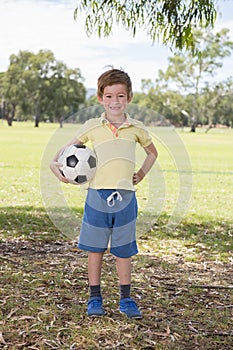 Young little kid 7 or 8 years old enjoying happy playing football soccer at grass city park field posing smiling proud standing ho