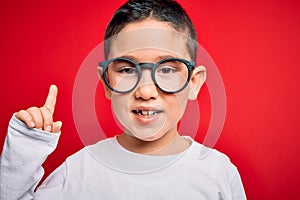 Young little smart boy kid wearing nerd glasses over red isolated background surprised with an idea or question pointing finger