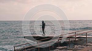 Young lonely boy walking at promenade. Sad man standing at pier. Melancholy boy looking at stormy ocean. Lonely boy coming to sea