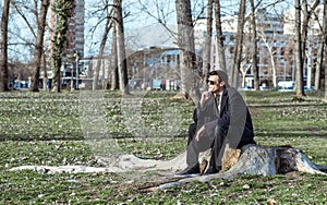 Young lonely depressed and anxious man sitting alone in the park on the wooden stump disappointed in his life crying and thinking