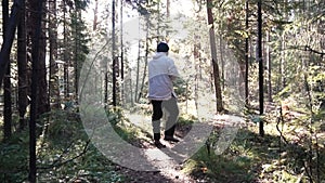 Young lonely man walking deep into forest among dense vegetation and bushes. Footage. View of man from back walking on