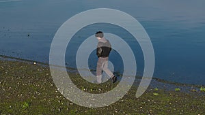 Young Lonely Man Walking On Lake Shore On Sunny Day. orbiting drone shot