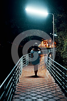 Young lonely woman walking on the bridge at night