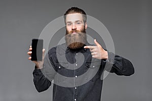 Young long bearded man pointed on camera screan of phone isolated on gray background