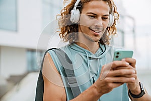 Young long-haired athletic smiling man in headphones using phone