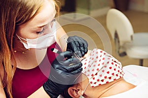 Young long-haired brunette woman putting false eyelashes on lady in beauty salon with masks