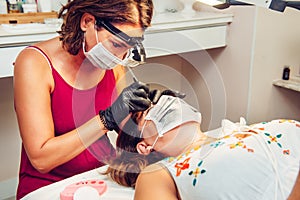 Young long-haired brunette woman putting false eyelashes on lady in beauty salon with masks