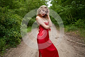 Young long-haired girl in a red dress posing in a summer park on the road. Women`s beauty, lifestyle, fashion