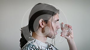 Young long-haired man drinking a glass of water, side view, loose ponytail