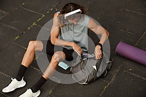 Young long-haired sporty man in headphones rummaging in bag