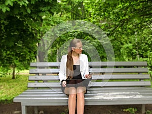 Young long-haired woman with glasses holds a mobile phone in her hand and a laptop on laps and looks away, front view. Adult