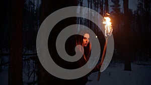 Young lost and scared woman with a fire torch walking in the night forest searching for the way out