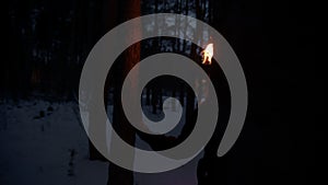 Young lost woman with a fire torch walking in the night forest and looking around