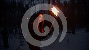 Young lost woman with a fire torch walking in the night forest searching for the way out