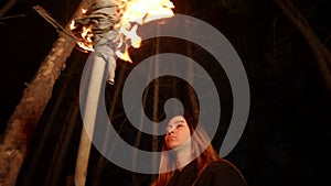 Young lost woman with long hair standing in winter forest at night with a handmade torch