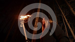 Young lost woman with long hair standing in winter forest at night with a handmade torch