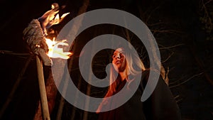 Young lost woman standing in dark winter forest with a handmade torch