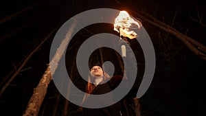 Young lost woman standing in scary winter forest at night with a handmade torch