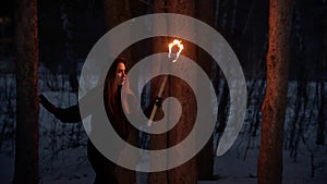 Young lost woman with torch walking in the night winter forest