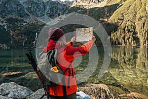 Young lost woman traveler with map and backpack relaxing outdoor with rocky on Morskie Oko lake. Woman traveler explorer