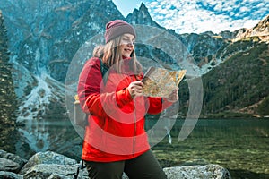 Young lost woman traveler with map and backpack relaxing outdoor with rocky on Morskie Oko lake. Woman traveler explorer