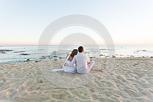 Young love couple sitting together on beach, rear view