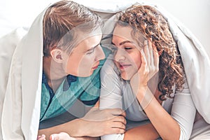 Young lovely couple in bed having fun covered with soft warm white blanket, Happy playful caucasian lovers relaxing in comfortable