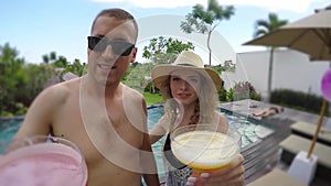 Young lovely couple clinking glasses near swimming pool at tropical vacation villa.